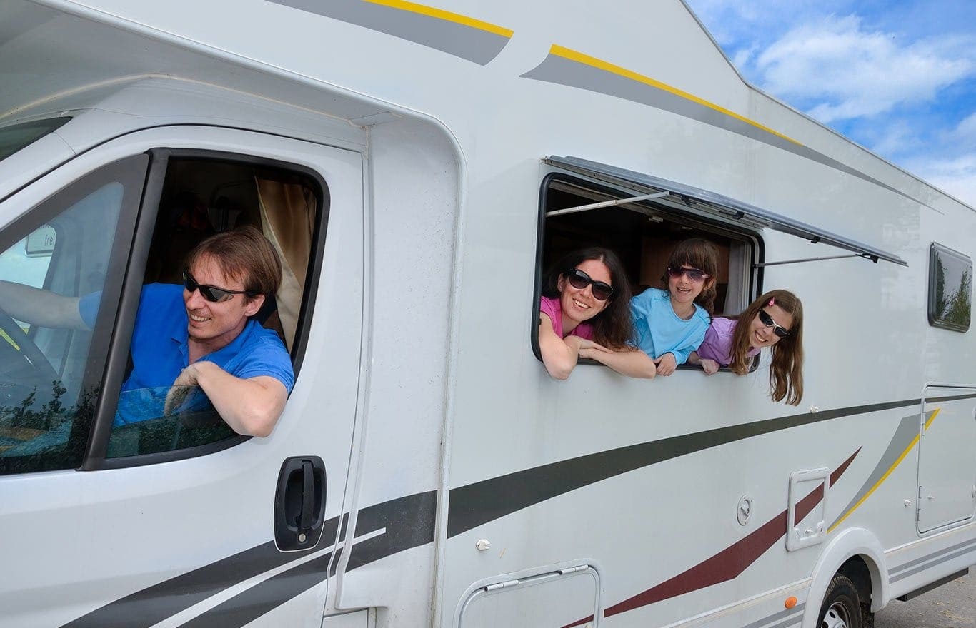 rates-page Four women leaning out of a white RV window, smiling and enjoying the day.